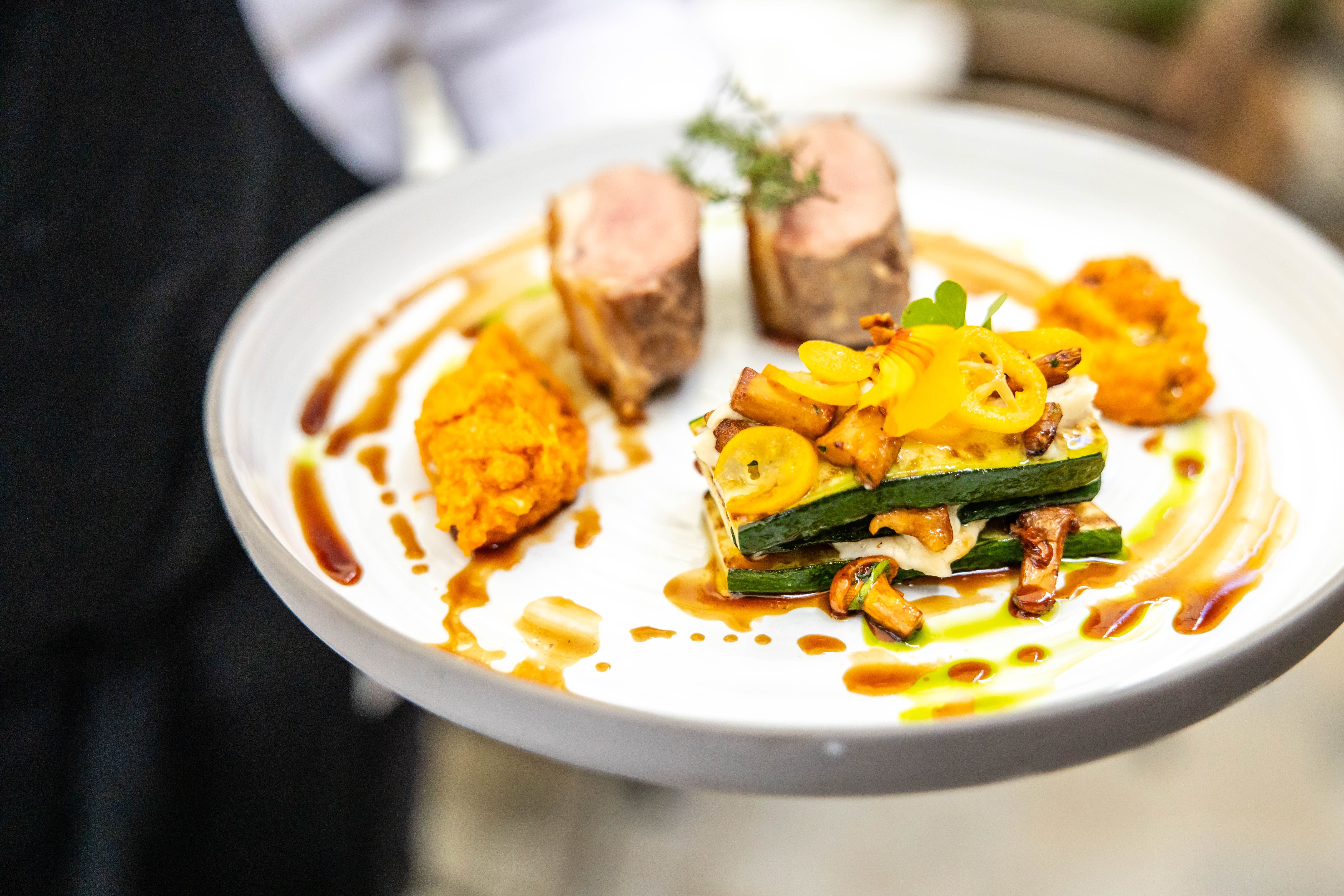 Gourmetgericht auf einem weißen Teller mit Fleisch, Gemüse und Soße.