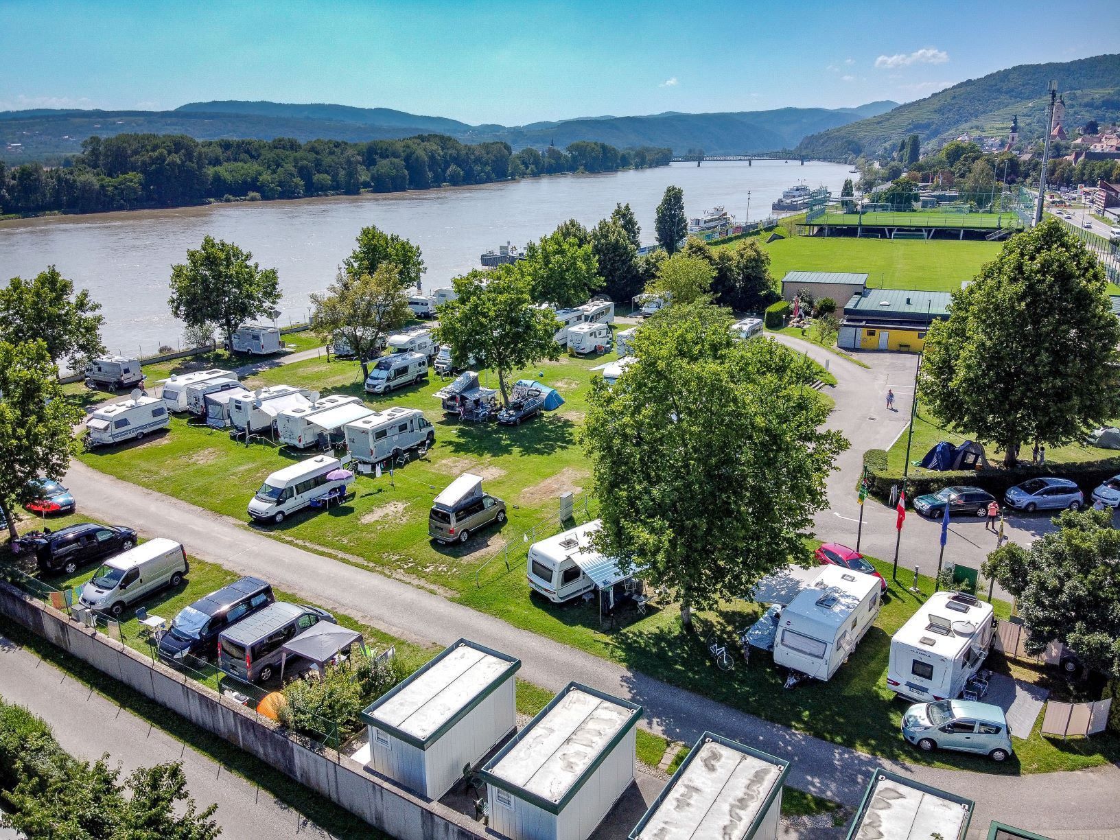Luftaufnahme eines Campingplatzes am Fluss mit Wohnmobilen und Zelten.