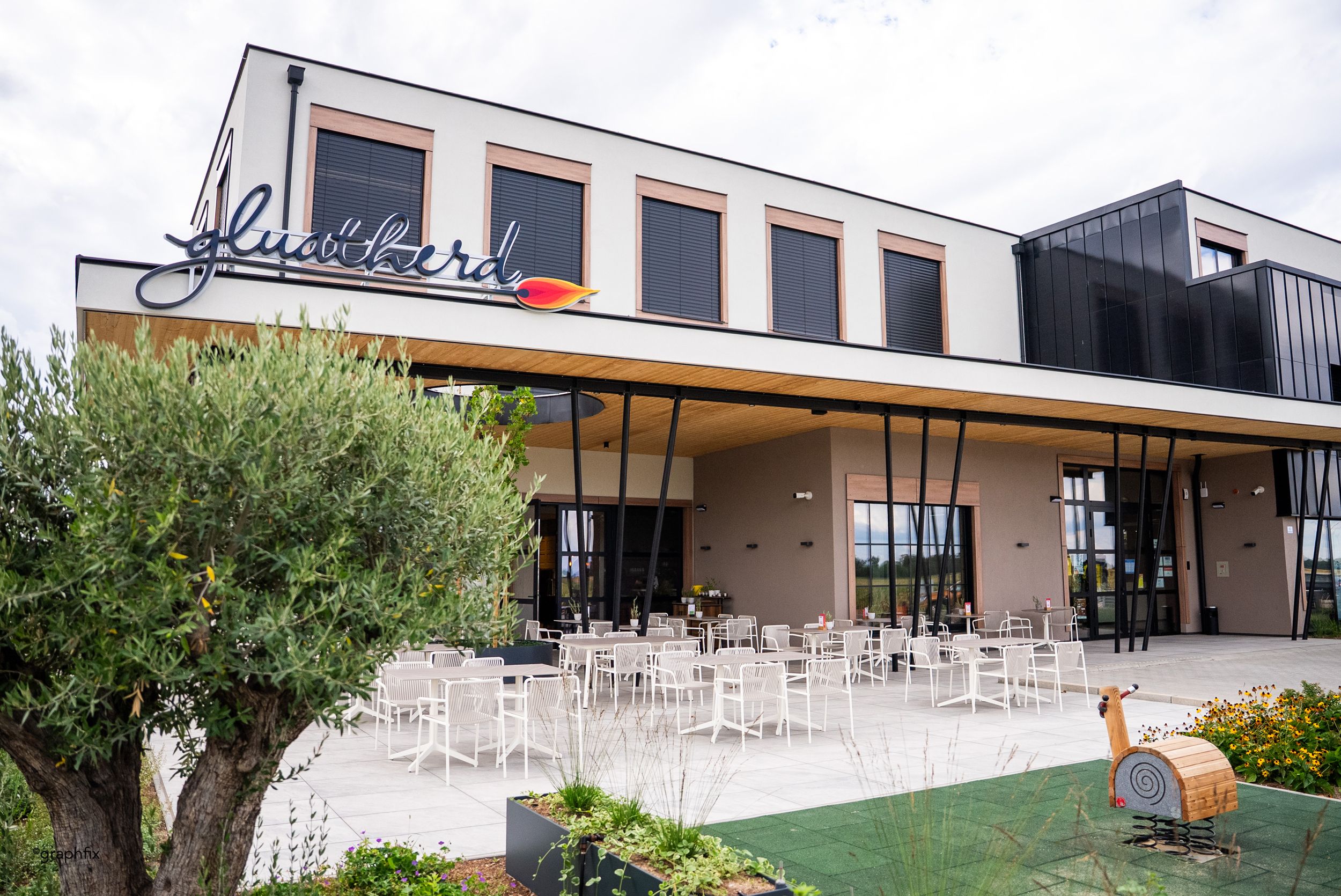 Außenbereich mit Tischen und Sesseln und einem Kinderspielplatz bei einem Restaurant.