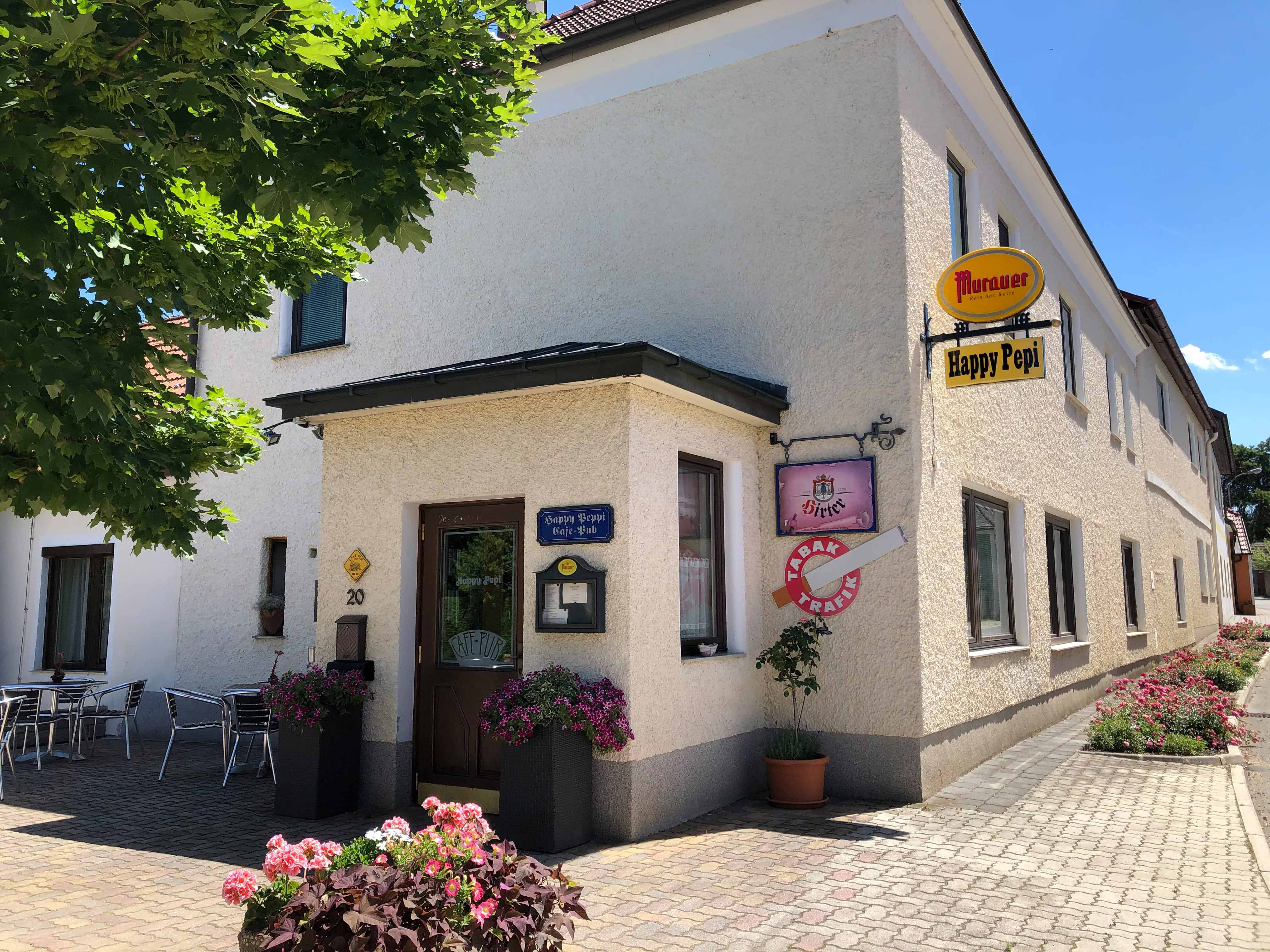 Außenansicht des Cafe Pub Happy Pepi mit Schildern und Blumendekoration.