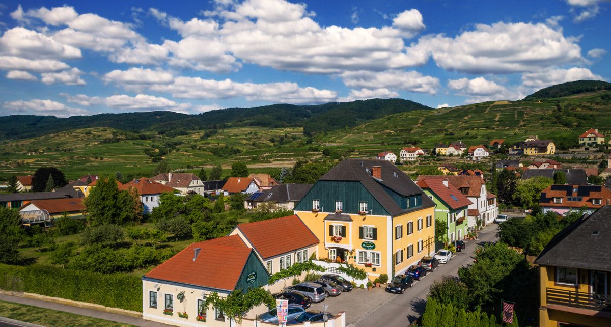 Ländliche Häuser in einer grünen Hügellandschaft unter blauem Himmel mit Wolken.
