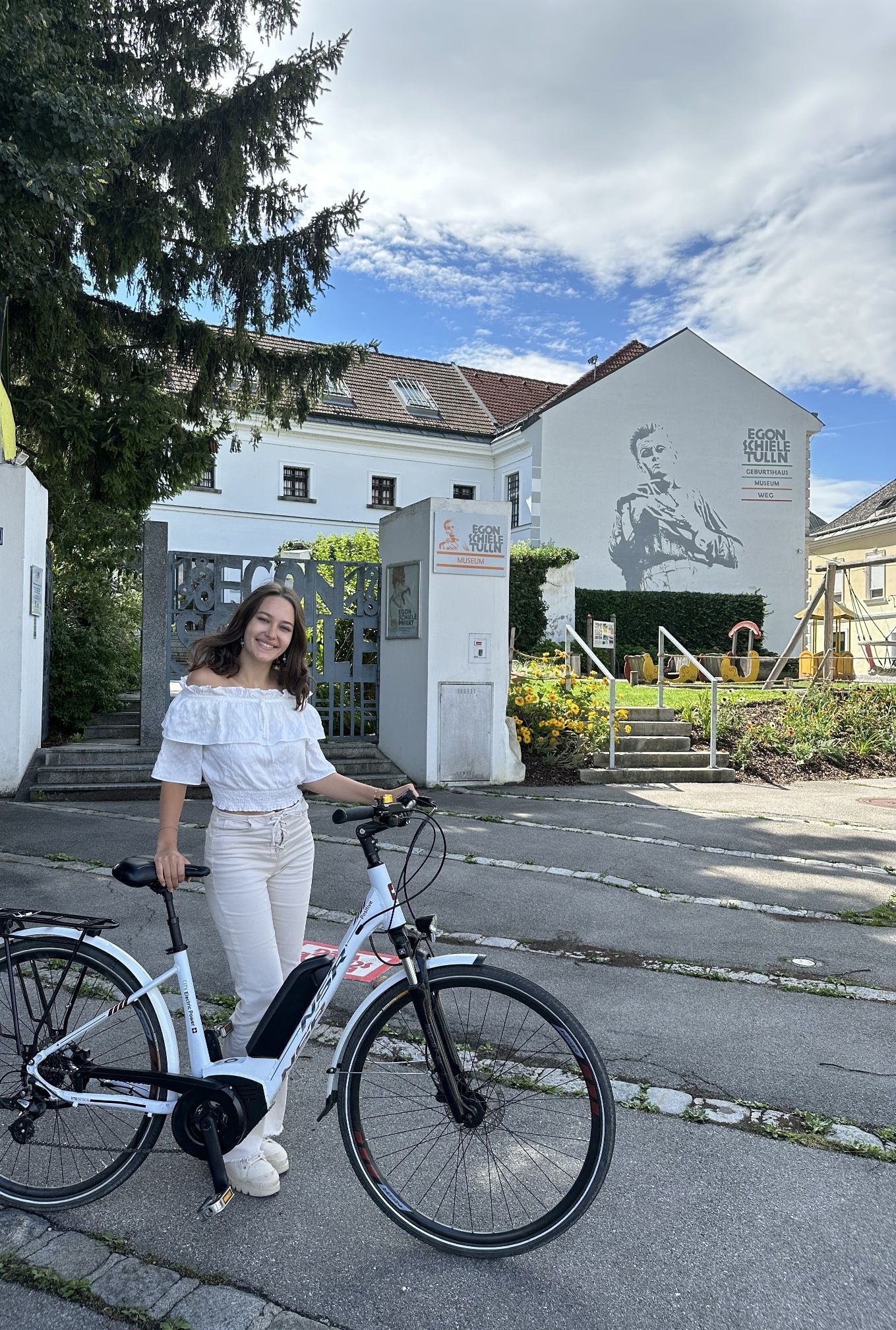 Eine Frau steht mit einem Fahrrad vor dem Egon Schiele Museum in Tulln, Österreich.