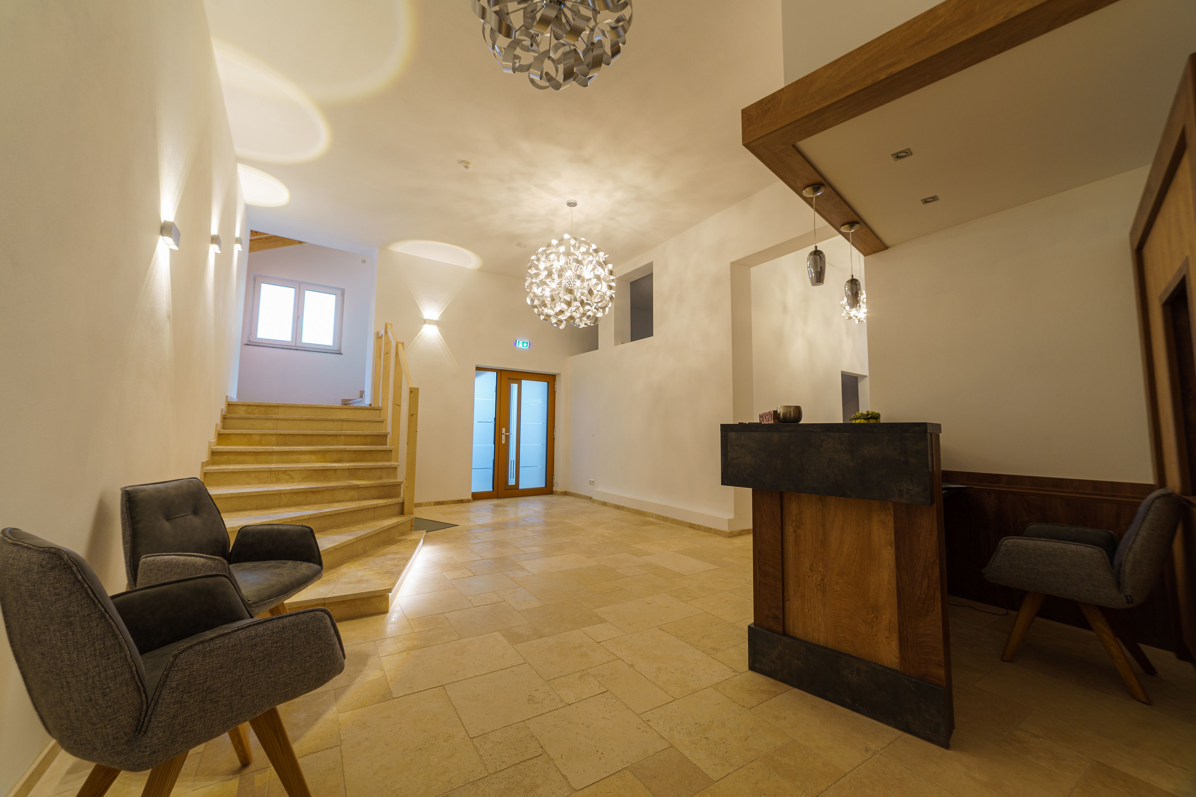 Moderne Rezeption mit Holztheke, zwei grauen Sesseln und Treppe.