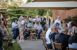 Viele Menschen sitzen dicht beieinander an Tischen im Freien vor der alten Scheune -  eine gesellige Stimmung unter Bäumen bei Tageslicht.