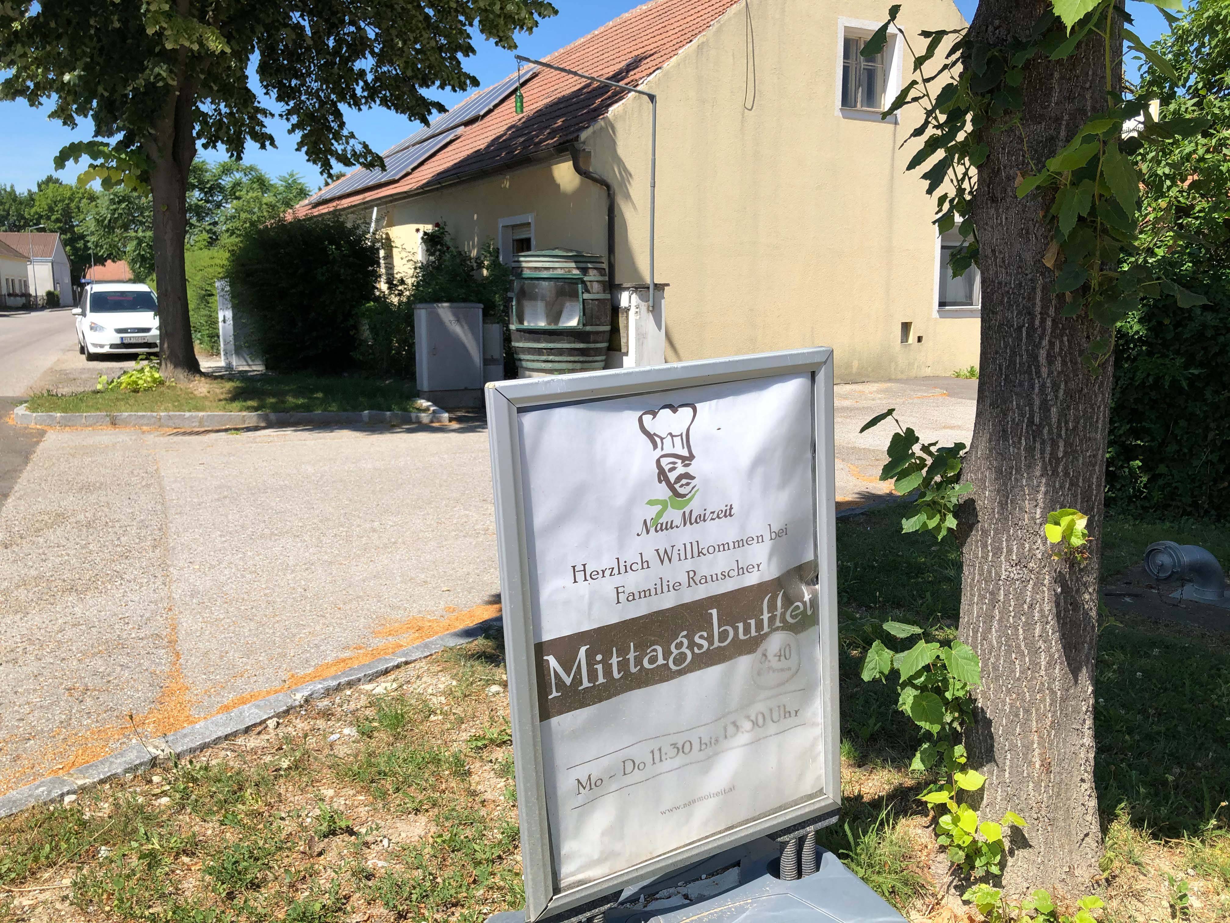 Ein Schild vor einem Gebäude mit der Aufschrift 'Mittagsbuffet' und 'Herzlich Willkommen bei Familie Rauscher'.