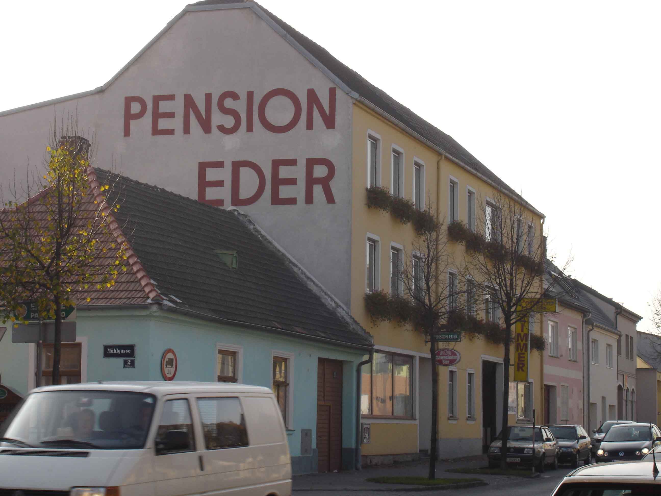 Straßenszene mit der Pension Eder und vorbeifahrenden Autos.