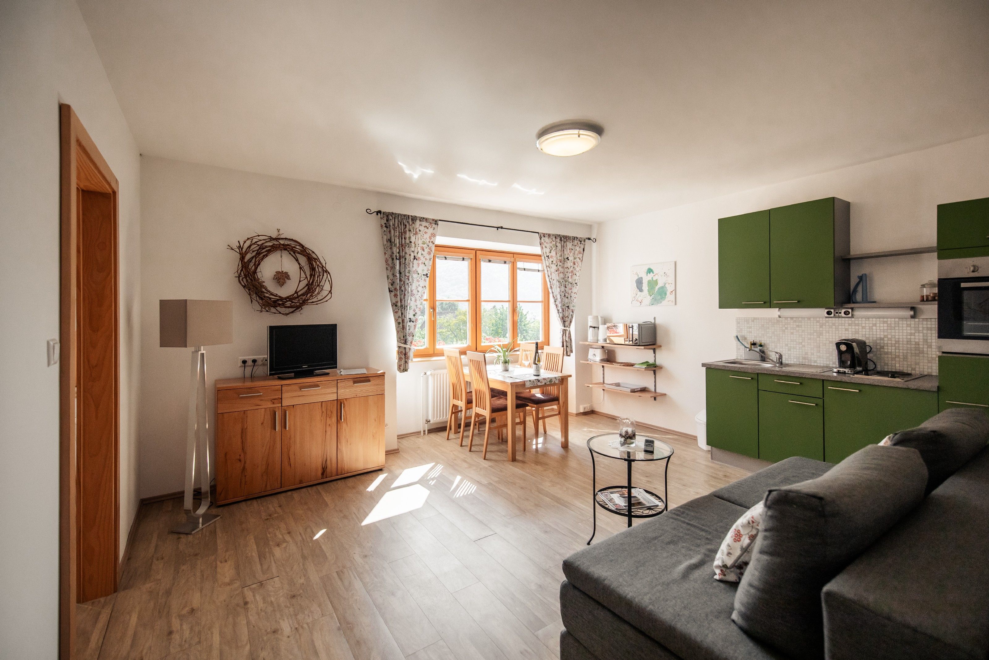 Helles Wohnzimmer mit grüner Küche, Esstisch und Sofa.