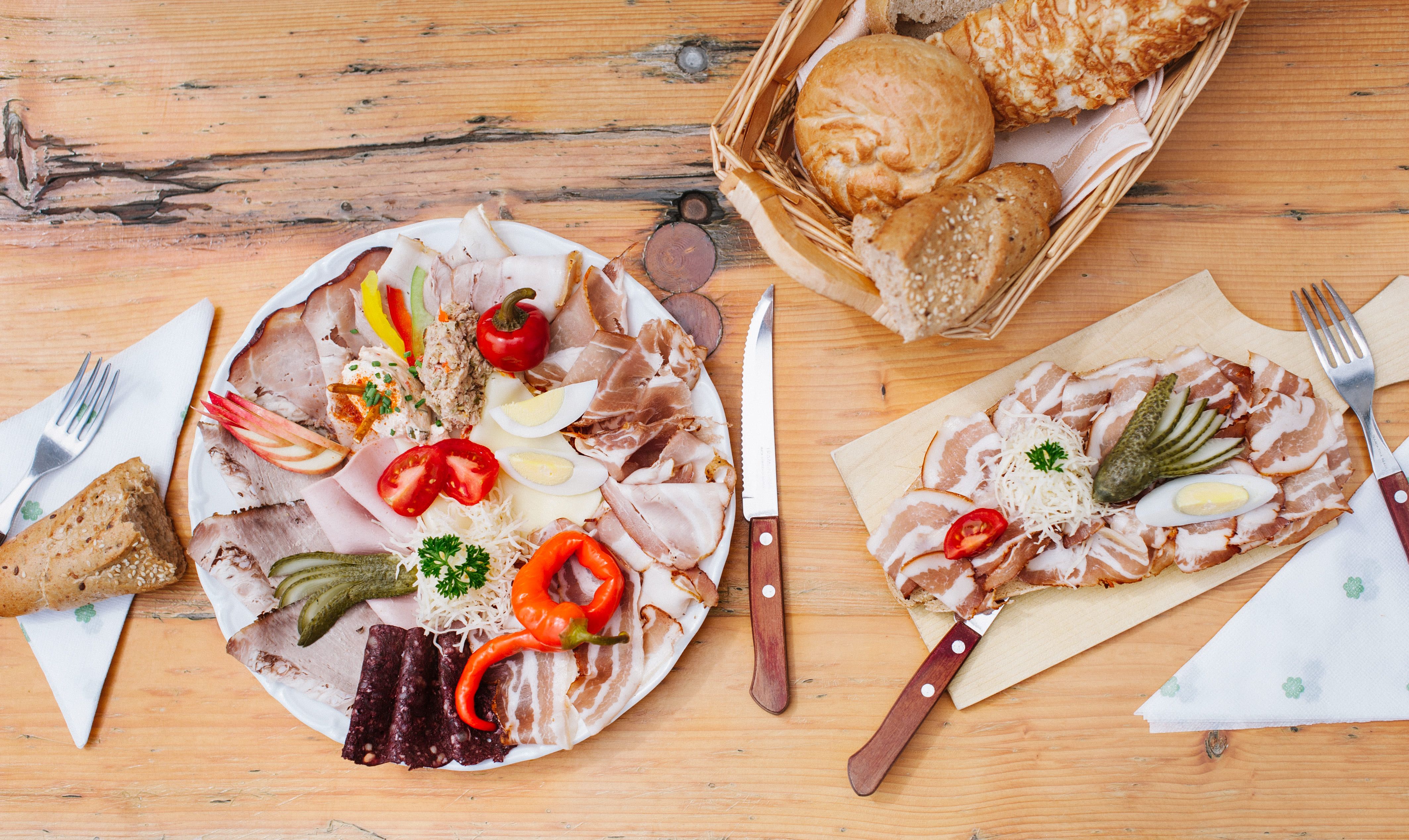 Brett mit Aufschnitt, Gemüse und Brot auf Holztisch.