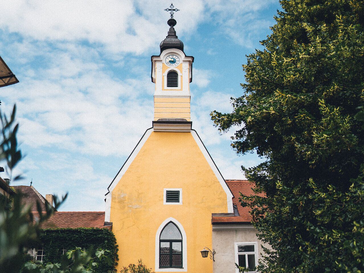 Die strahlend gelbe Fassade des Nikolaihofs zieht die Blicke auf sich und strahlt eine einladende Atmosphäre aus. Umgeben von üppigem Grün und blühenden Pflanzen, bietet dieser Ort eine perfekte Kulisse für Weinliebhaber und Naturliebhaber gleichermaßen. Hier, wo die Donau sanft fließt, erleben Besucher die Harmonie von Tradition und Natur.