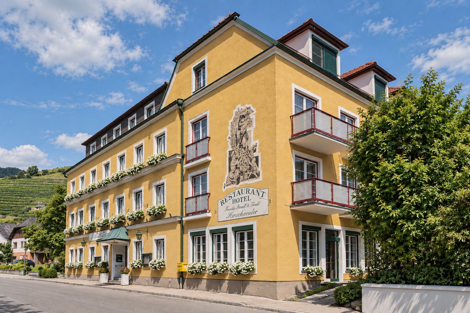 A Wachau-völgyben található Wachau borhotel külső képe: sárga homlokzat, erkélyek, virágok és az étterem táblája.