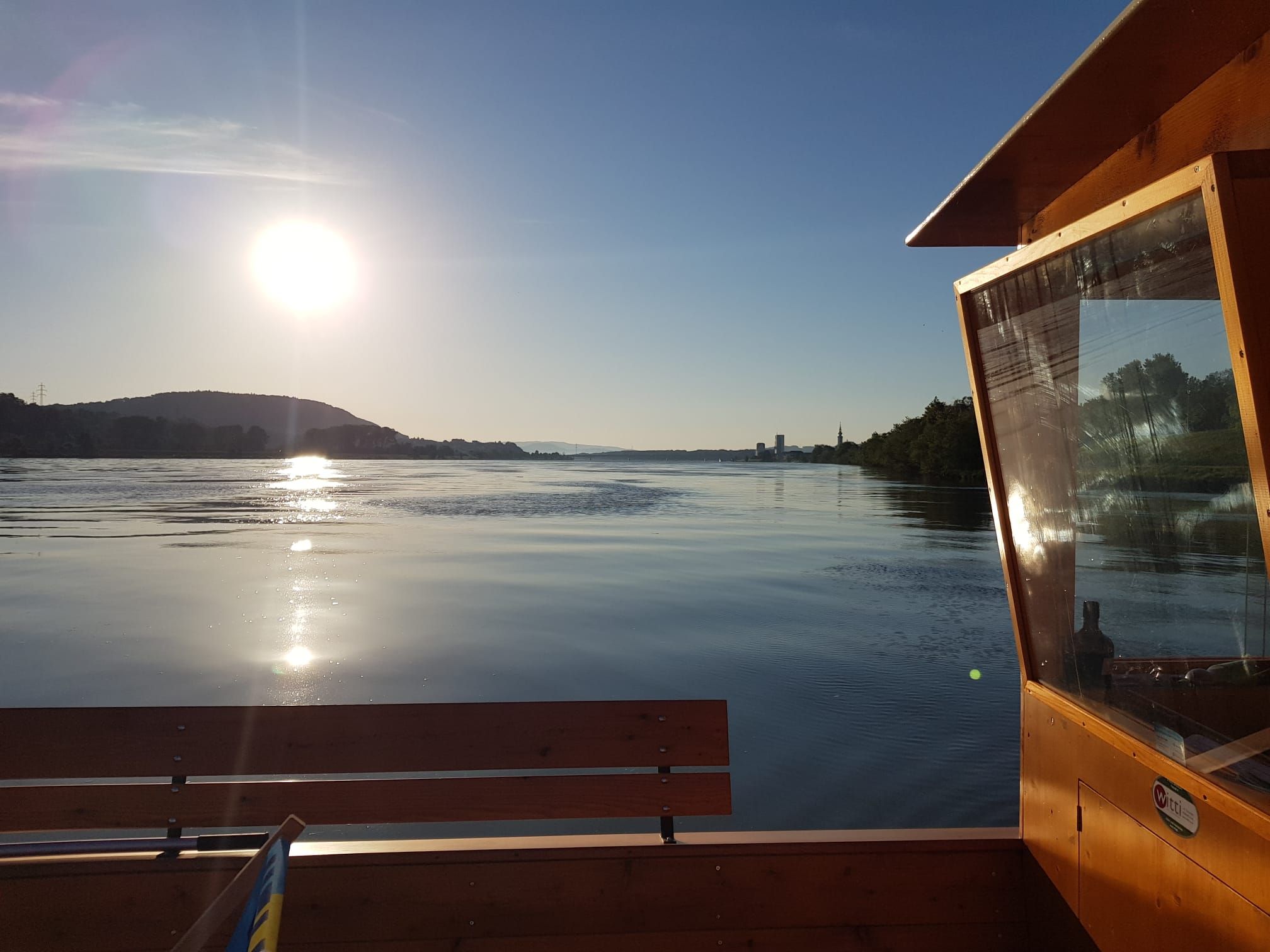 Sonnenuntergang über einem ruhigen Fluss mit einem Holzboot im Vordergrund.