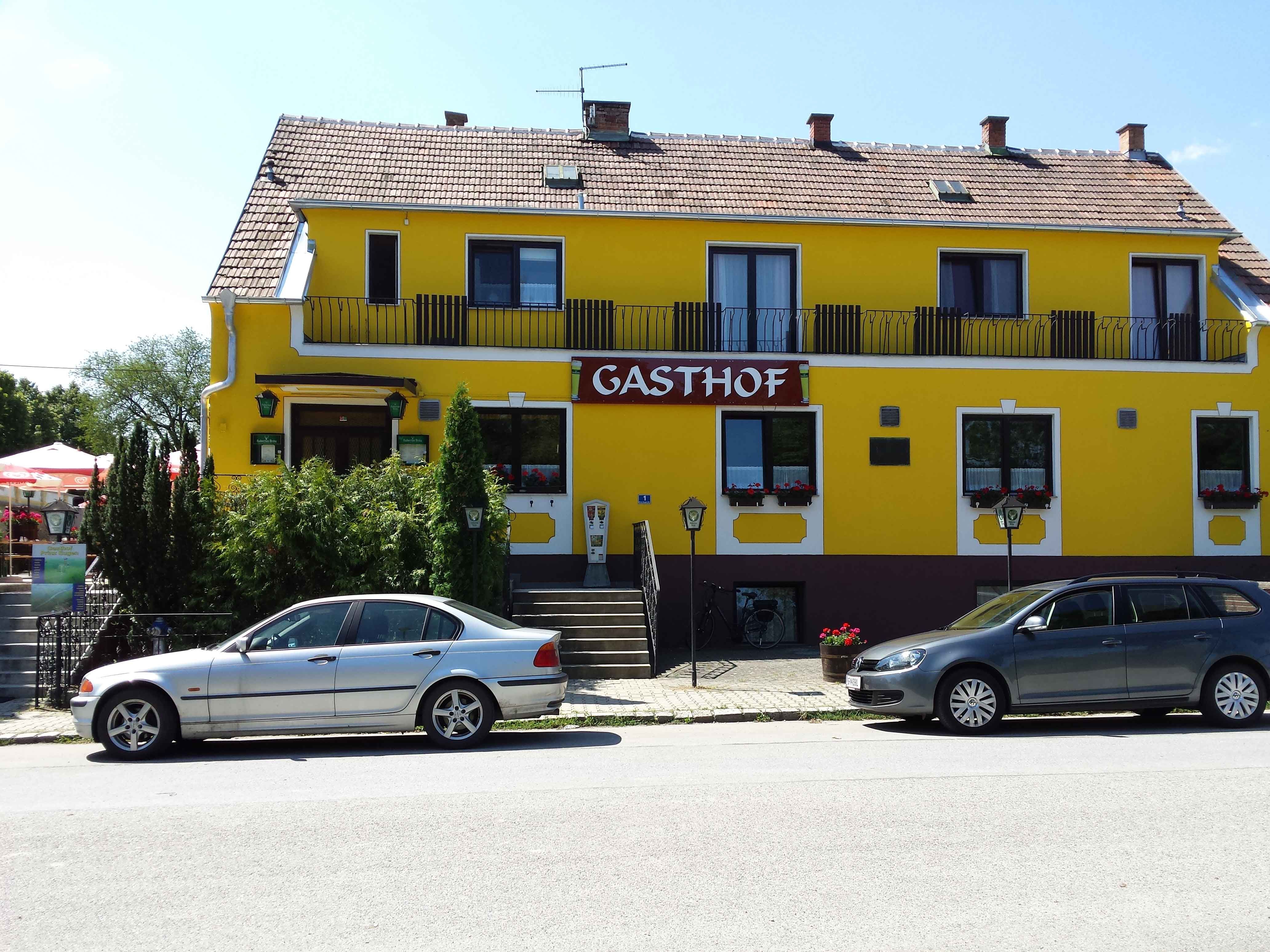 Gelbes Gebäude mit der Aufschrift 'Gasthof', zwei geparkte Autos davor.