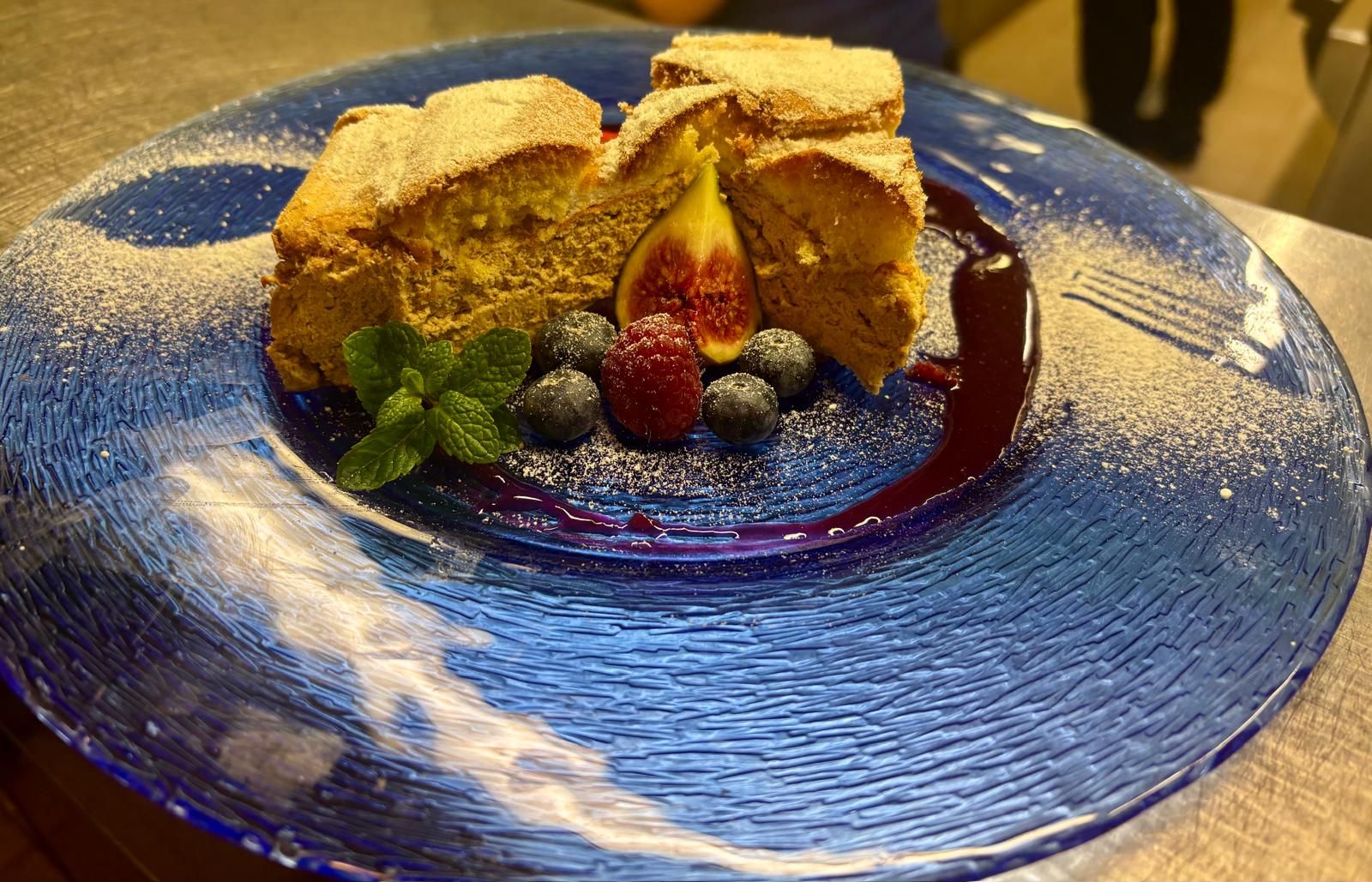 A dessert on a blue plate, decorated with berries, figs and mint leaves, dusted with powdered sugar.
