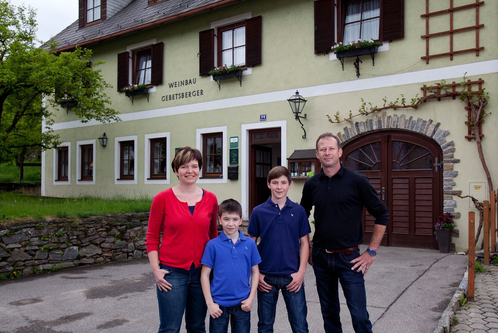 Eine Familie steht vor einem Gebäude mit der Aufschrift 'Weinbau Gebetsberger'.