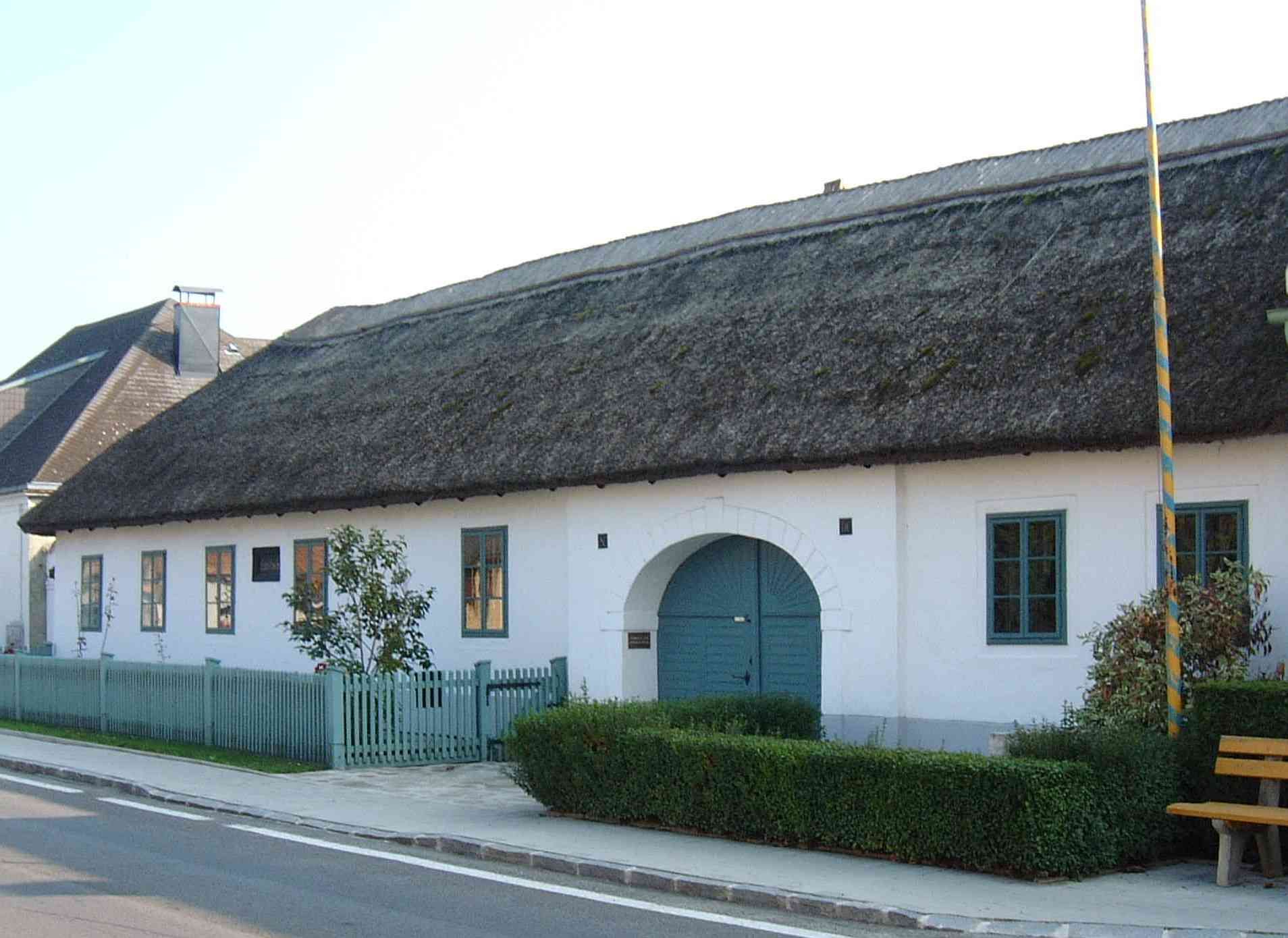 Das Geburtshaus von Joseph Haydn in Rohrau, Österreich, mit Strohdach und blauen Fenstern.