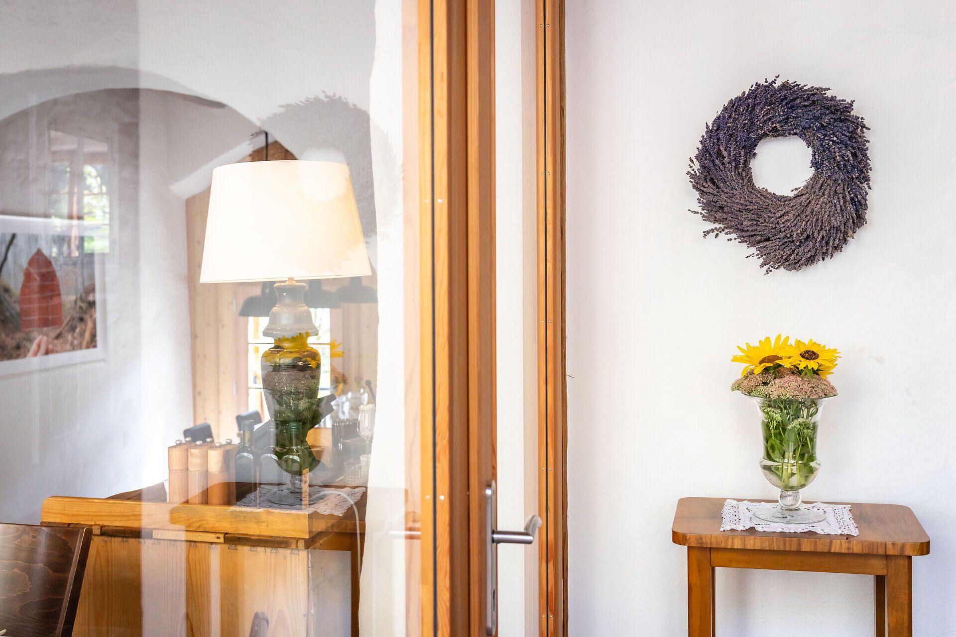 Auf einem kleinen Holztischchen steht eine Vase mit Sonnenblumen und darüber ein Lavendelkranz. 